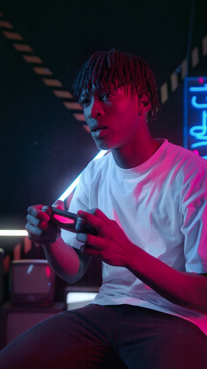 A young man plays video games with a controller in a neon-lit room, showcasing modern gaming culture.