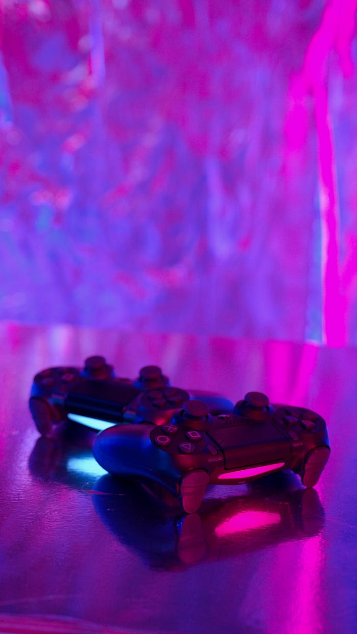 Artistic shot of two gaming controllers on a reflective surface with vibrant neon lighting.